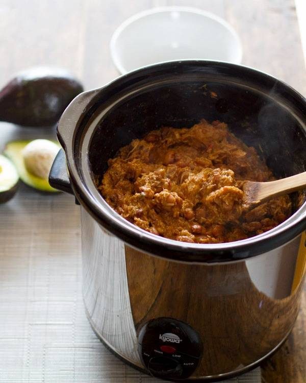 Chicken in a crockpot with a wooden spoon.