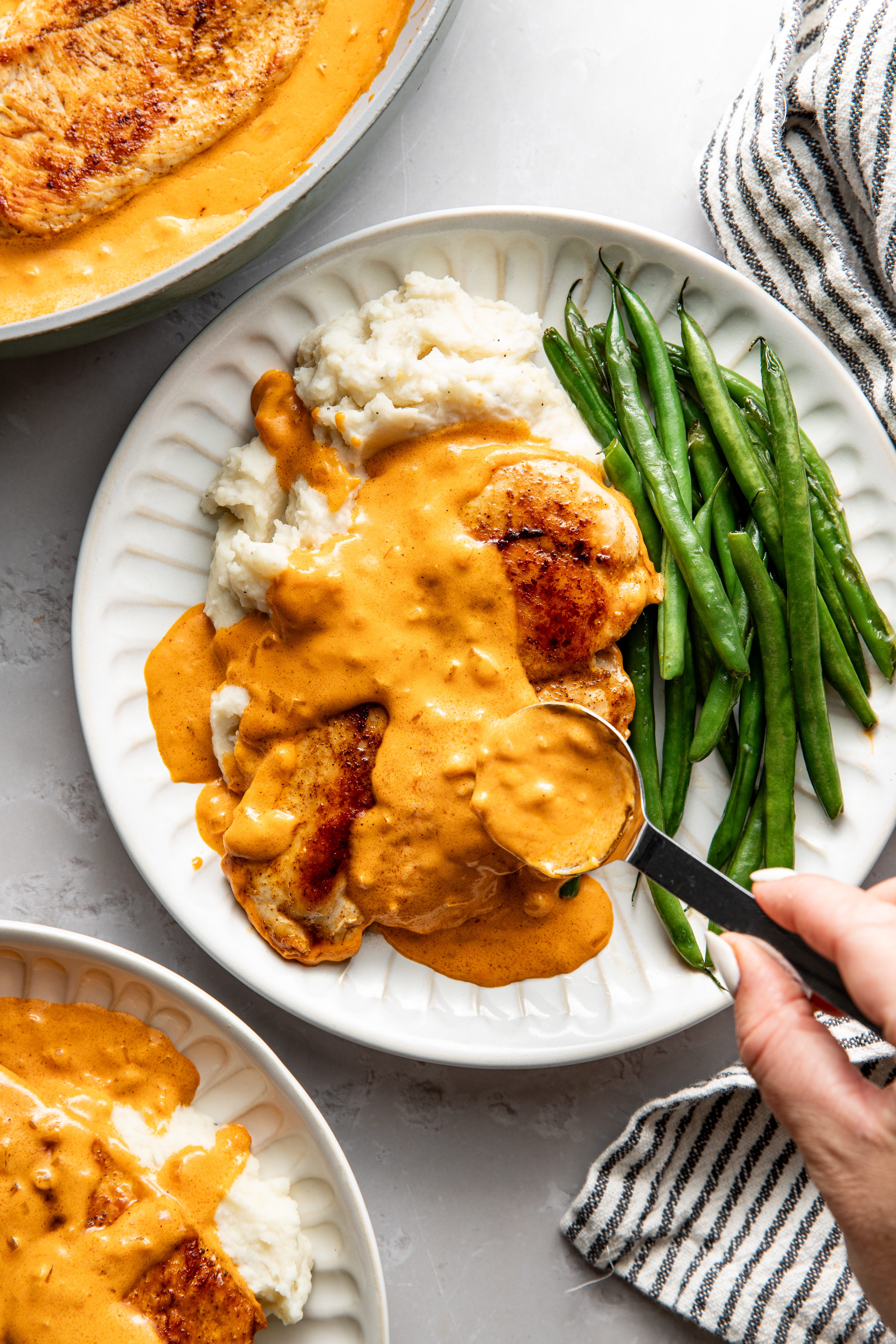 Pouring sauce over chicken on a plate.