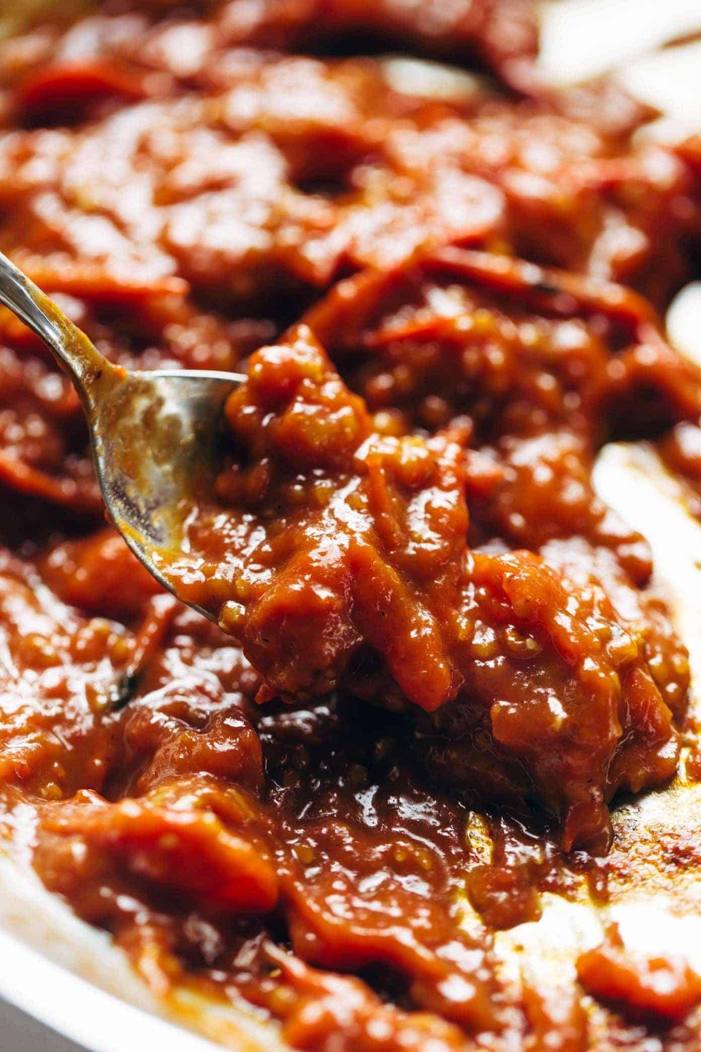 A spoon reaches into a tomato sauce.
